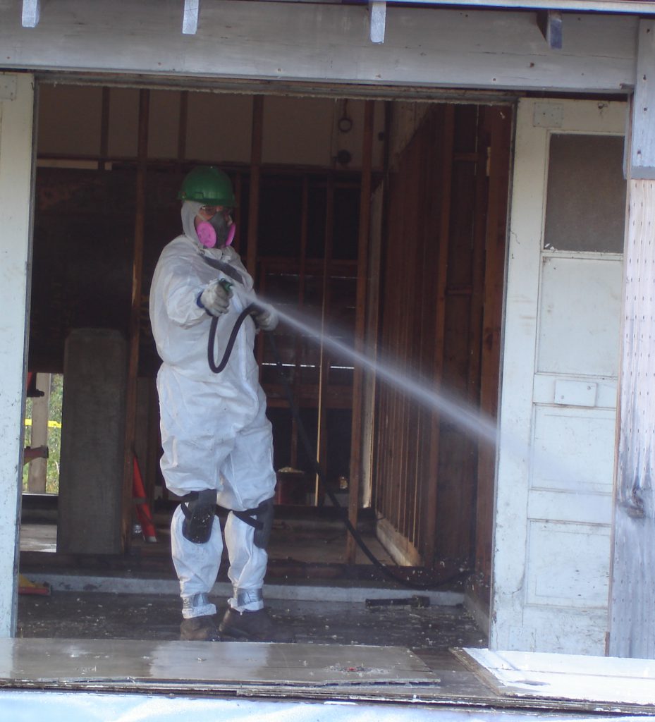 man with hazmat gear spraying down building
